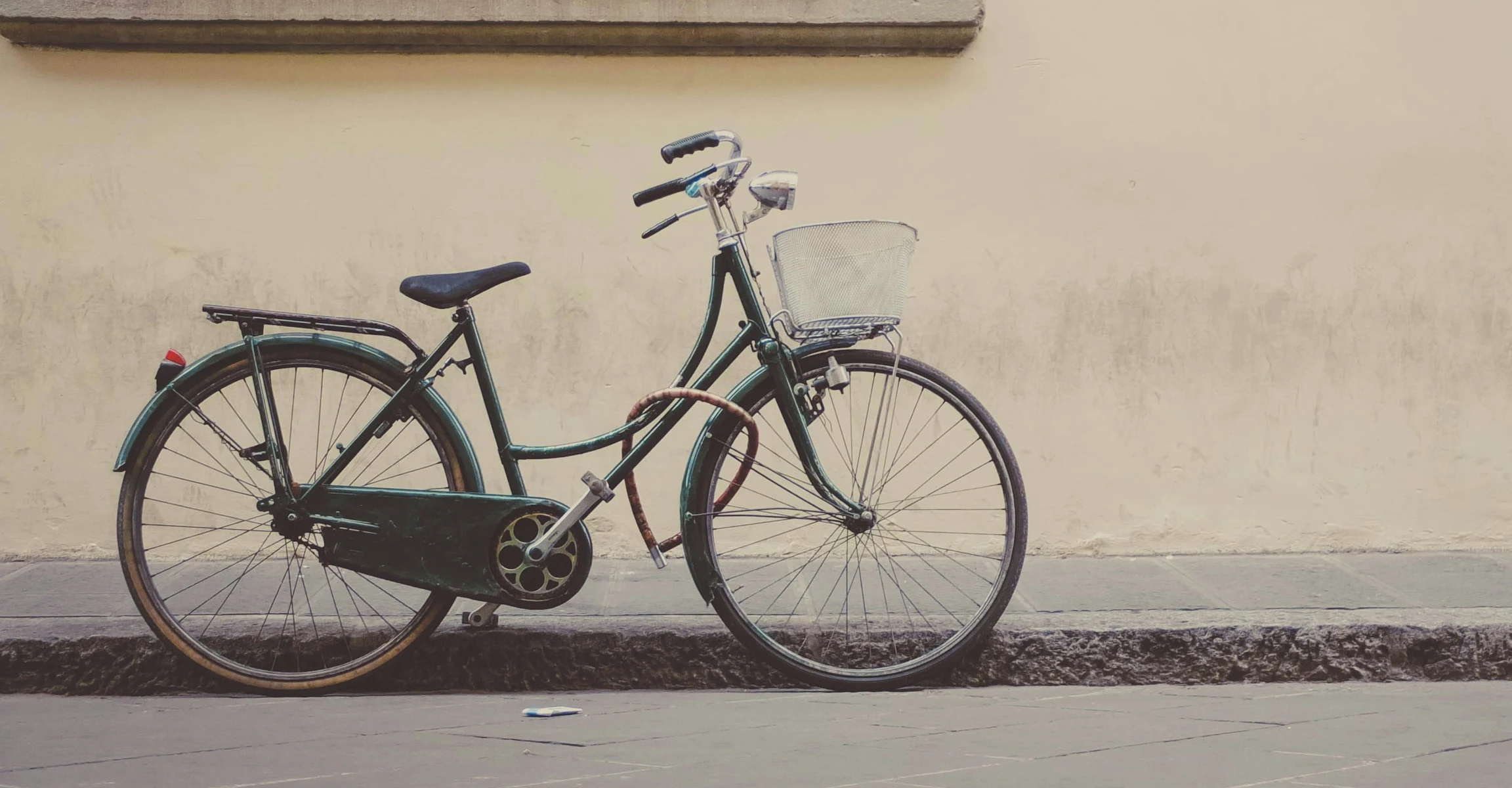 A dark city bicycle with a low open frame, front basket and enclosed chain.